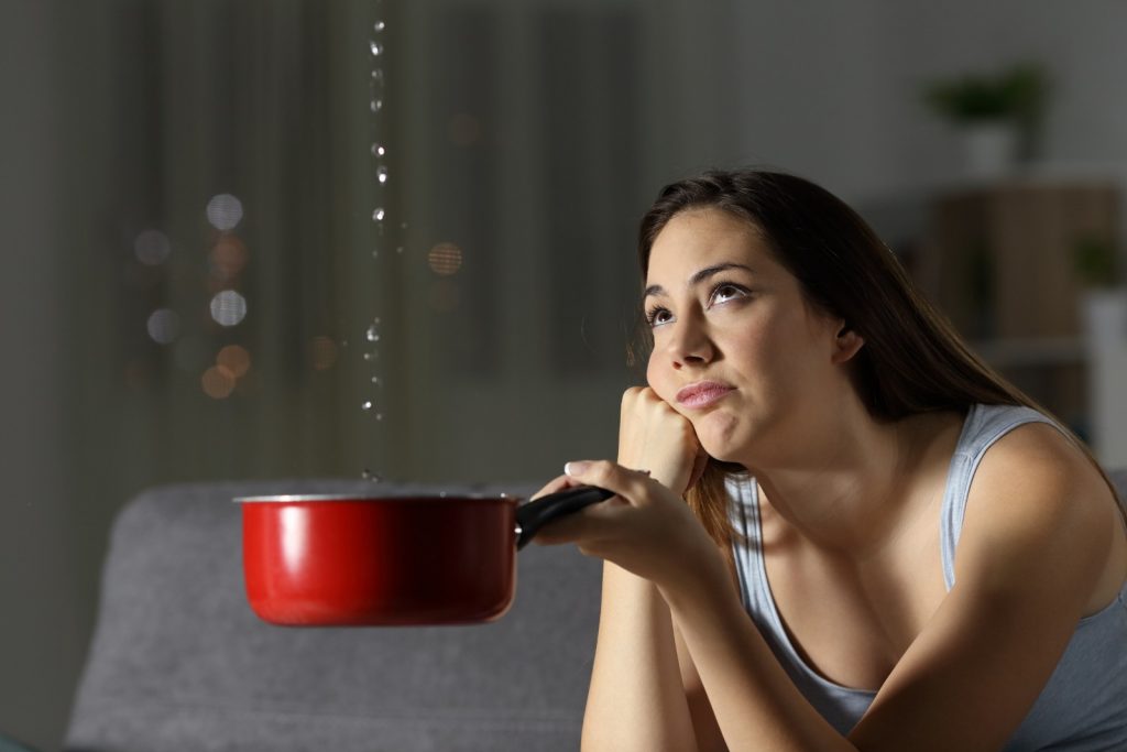 Frustrated woman looking at roof water leaks while holding a pot to catch drops of water